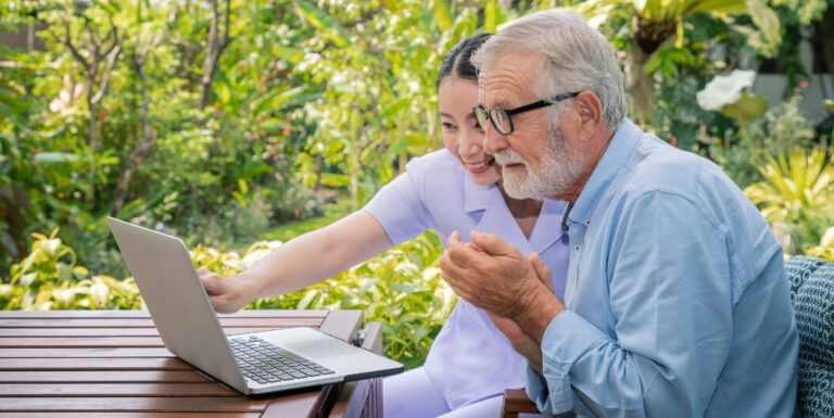 Female Nurse Helping Elderly Man Learn a Language on Laptop at Independent Living Facility