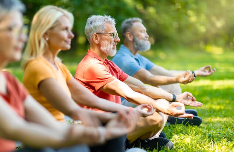 Elderly Adults Meditating Together on the Grass at an Independent Living Community